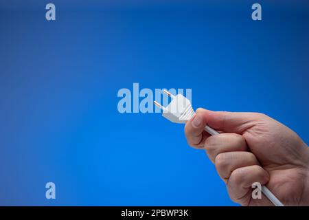 European style electric socket and cord held in hand by male hand. Close up studio style, isolated on blue background. Stock Photo