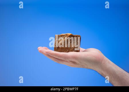 Old style homemade artisanal soap bar held in male palm. Close up studio shot, isolated on blue background. Stock Photo