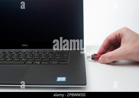 USB memory stick or charger cable being inserted into laptop port by Caucasian male hand. Close up studio shot, isolated on white background. Stock Photo