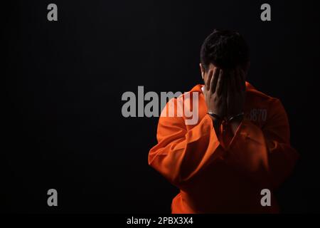 Prisoner in jumpsuit with handcuffs on black background, space for text Stock Photo