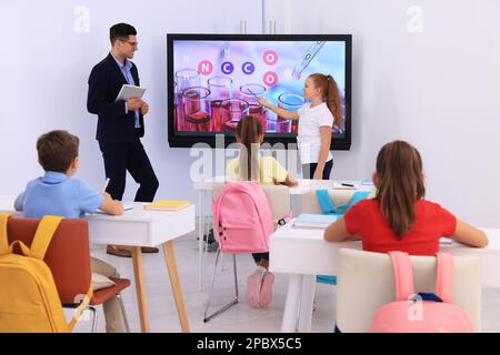 Teacher and pupil using interactive board in classroom during lesson Stock Photo