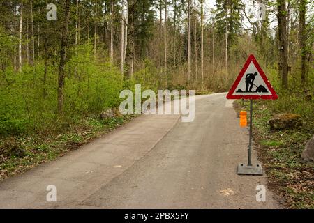 Road works warning road sign on a dirt road in the forest. Day time, no people. Stock Photo
