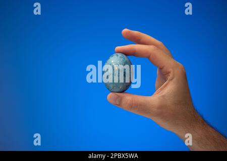 Hand painted and decorated blue easter egg held in hand by Caucasian male. Close up studio shot, isolated on blue background. Stock Photo