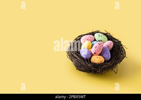 Colorful Easter eggs inside a nest on yellow background. Copy space Stock Photo