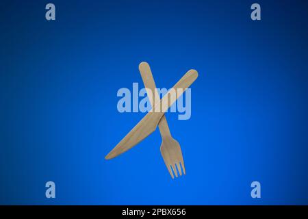 Single use disposable and biodegradable wooden knife and fork. Close up studio shot, isolated on blue background. Stock Photo