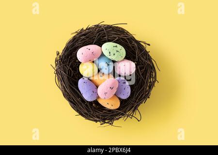 Colorful Easter eggs inside a nest on yellow background. Copy space Stock Photo