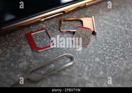 SIM card, mobile phone, tray and ejector tool on grey table, closeup Stock Photo