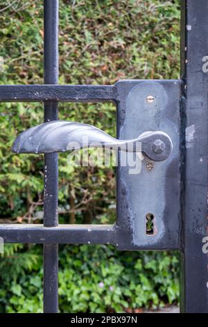 Old weathered vintage forged metal gate lock with green defocused vegetation in the background. Close up front view, shallow depth of field, no people Stock Photo