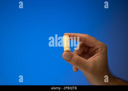 One golden corn puff held in hand by Caucasian male hand. Close up studio shot, isolated on blue background. Stock Photo