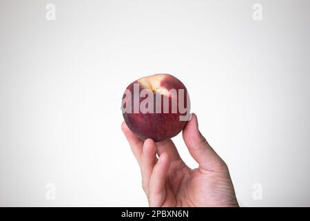 Fresh ripe peach held in hand by Caucasian male hand. Close up studio shot, isolated on a white background. Stock Photo