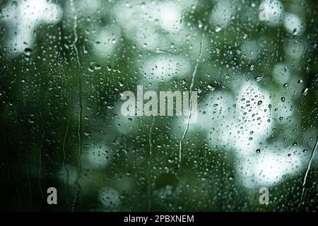 Raindrop running down a car windshield glass. Close up shot, shallow depth of field, green nature background, no people Stock Photo