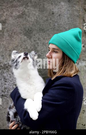 Pondering female owner in warm clothes looking away with adorable Husky dog on hands while spending time in winter nature Stock Photo
