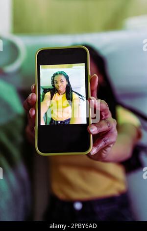 Top view of calm young black female in casual clothes taking photo on smartphone while lying on sofa at home Stock Photo