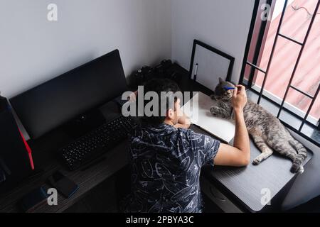 High angle back view of unrecognizable male freelance photographer sitting at wooden desk near computer and profession photo camera while caressing ad Stock Photo