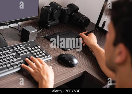 From above of crop unrecognizable male photographer sitting at wooden table with professional photo camera while retouching photos on graphics tablet Stock Photo
