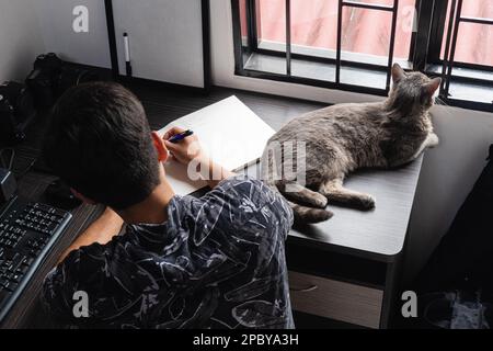 High angle back view of unrecognizable male freelance photographer sitting at wooden desk with computer while writing on white paper camera near adora Stock Photo