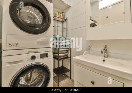Modern bathroom with washing machine and dryer placed near shelves with towels and sink on cabinet under mirror in light apartment Stock Photo