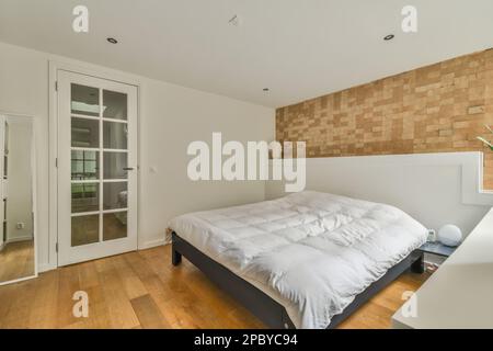 Comfortable bed with soft blanket placed near window and brick wall in light bedroom interior with minimalist style Stock Photo