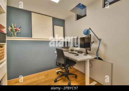 Desk with computer monitor and mouse placed near lamp and laptop against shelves and pictures on shelf in modern home office with chair Stock Photo