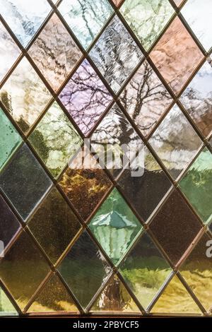 Backyard view with street lamp and trees against building and gloomy sky through multicolored dusty stained glass window in autumn Stock Photo