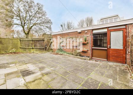 Exterior of residential building with brick construction and green plants hanging on wall against wooden fence under blue sky Stock Photo