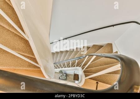 From above of spiral brown stairway with metal railings in light house with white walls Stock Photo