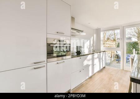 Interior of stylish open plan kitchen with white cabinets and built in appliances on open plan room Stock Photo
