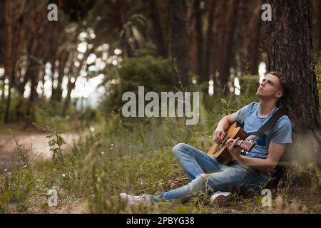 Pensive man playing guitar forest concept. Stock Photo