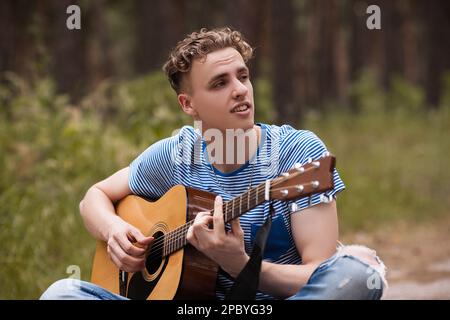 Smiling man playing guitar forest concept. Stock Photo