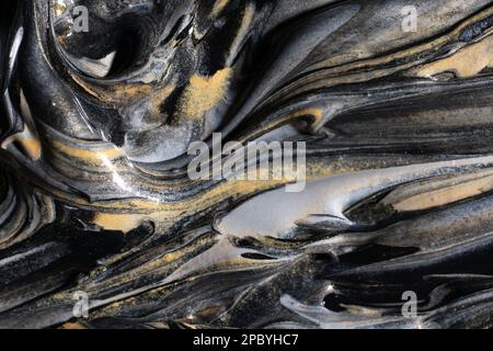 Spills of shiny golden and silver dye mixing with black pigment Stock Photo