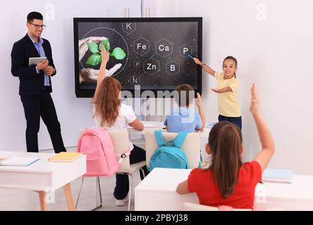 Teacher and pupil using interactive board in classroom during lesson Stock Photo