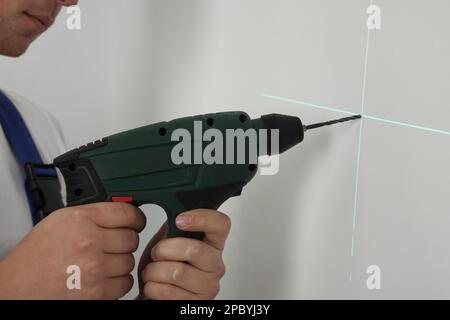 Man using cross line laser level for accurate measurement and drilling hole in light wall, closeup Stock Photo