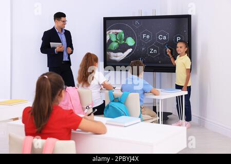 Teacher and pupil using interactive board in classroom during lesson Stock Photo