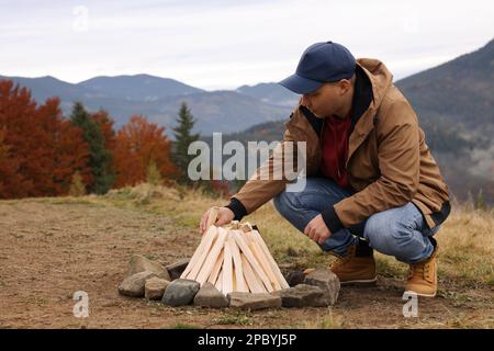 Young man making bonfire in mountains. Camping season Stock Photo