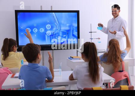 Teacher holding flask with solution near interactive board in classroom during practical lesson Stock Photo