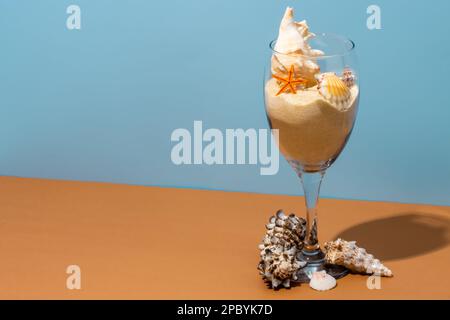 High angle of transparent glass filled with sand decorated with various sized conches and starfish placed on beige table near blue wall Stock Photo