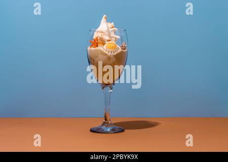 Transparent wineglass filled with loose sand decorated with assorted seashells and starfish placed on table and casting shadow Stock Photo