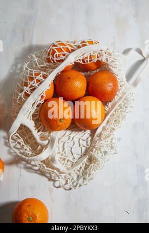 Top view of fresh unpeeled bloody oranges placed in reusable white mesh bag on table Stock Photo