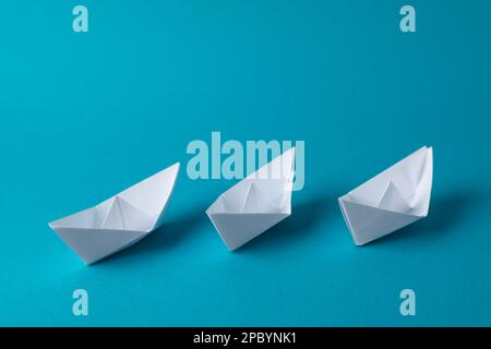 Handmade white paper boats on light blue background.  Origami art Stock Photo