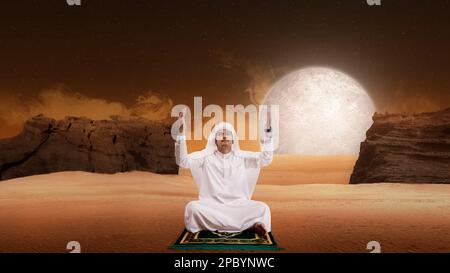 Muslim man sitting while raised hands and praying in the desert Stock Photo