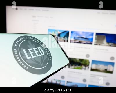 Cellphone with logo of US green building certification LEED on screen in front of website. Focus on right of phone display. Stock Photo