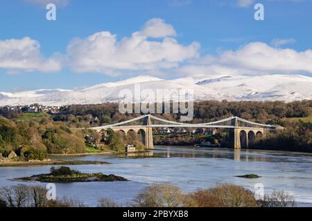 Scenic view to Menai Suspension bridge crossing Menai Strait with snow on mountains in winter. Menai Bridge (Porthaethwy), Isle of Anglesey, Wales, UK Stock Photo