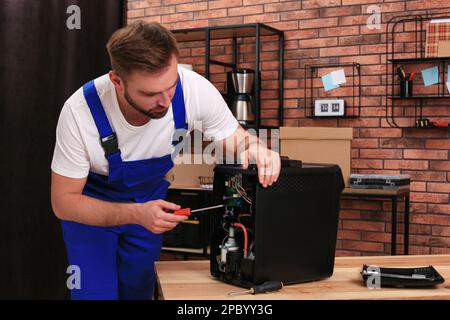 Repairman with screwdriver fixing coffee machine at table indoors Stock Photo