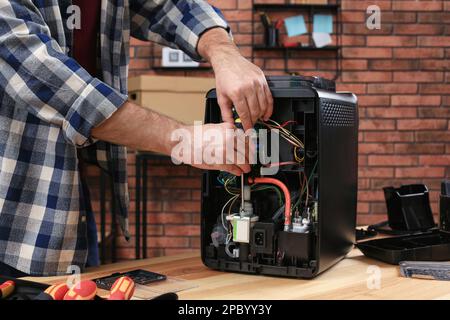 Man with screwdriver fixing coffee machine at table indoors, closeup Stock Photo