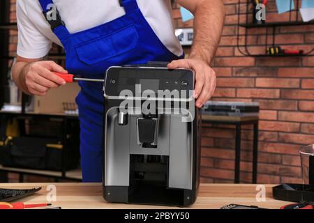 Repairman with screwdriver fixing coffee machine at table indoors, closeup Stock Photo