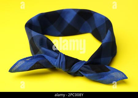 Tied blue checkered bandana on yellow background, closeup Stock Photo