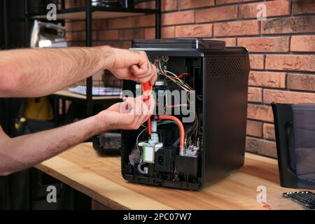 Repairman with screwdriver fixing coffee machine at table indoors, closeup Stock Photo