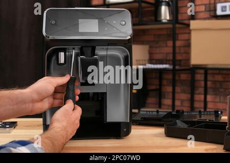 Man with screwdriver fixing coffee machine at table indoors, closeup Stock Photo