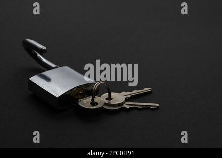 Open steel padlock with three keys on black surface Stock Photo