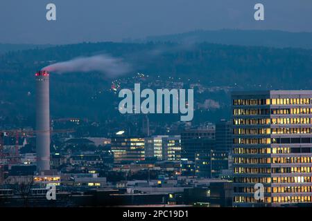 Tall smokestack or industrial chimney emitting white smoke or steam. Zurich city Switzerland. Late evening winter day, close-up telephoto shot.. Stock Photo